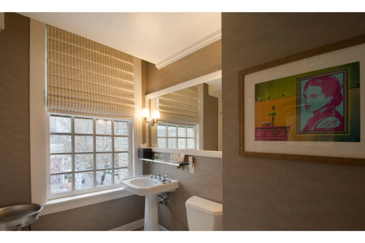 A serene bathroom space with a stylish sink and mirror, accented by artwork and natural light streaming from a window. The overall mood is peaceful and artistic, perfect for quiet moments of solitude and self-care.