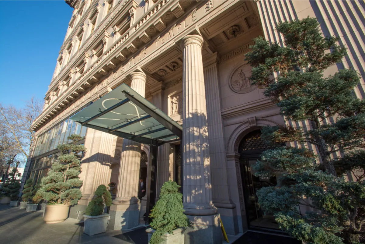 A stately exterior shot showing the grand entrance of a historic building with ornate columns, a welcoming canopy, and beautifully landscaped shrubs. The architecture hints at the property’s rich heritage and offers a sense of arrival.