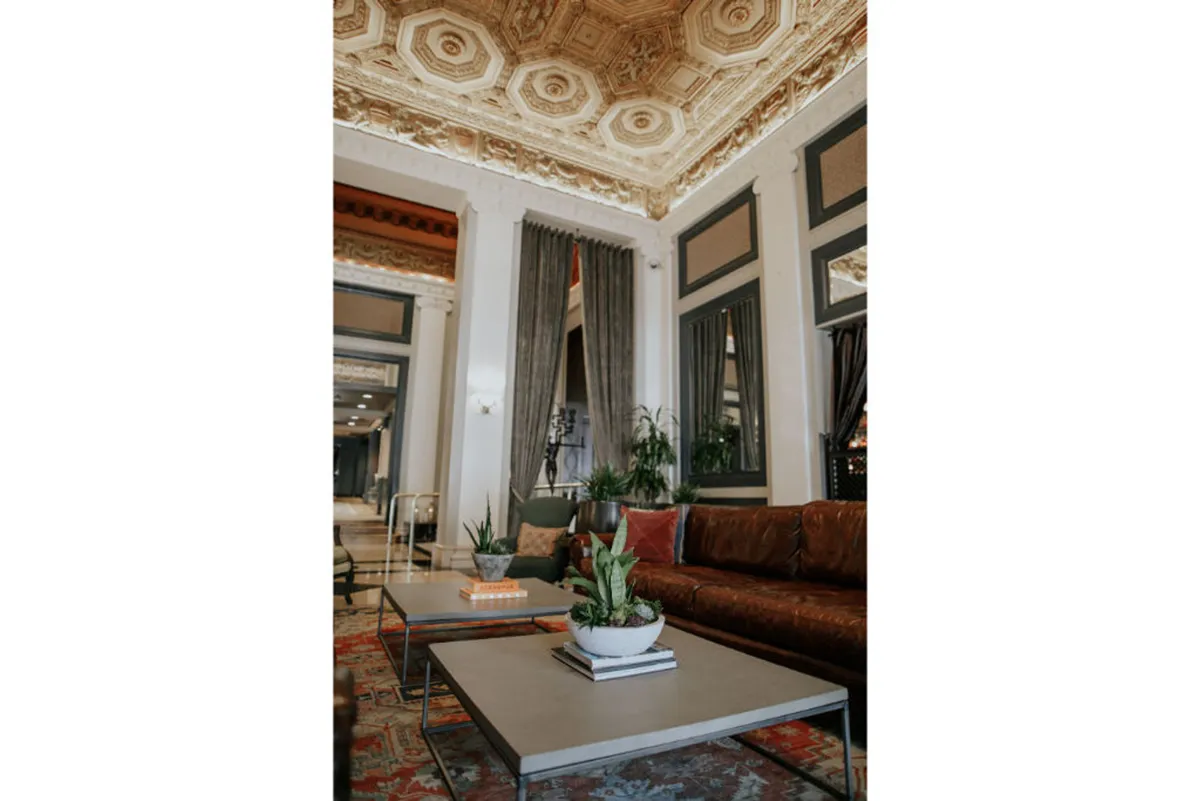 An inviting and stylish lounge with comfortable leather sofas, elegant coffee tables, decorative plants, and an ornate ceiling—set for guests to relax, socialize, or enjoy quiet moments.