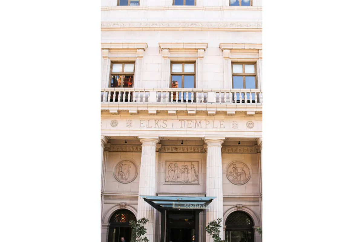A detailed exterior shot of the Elks Temple inscription, ornate columns, and decorative reliefs that underscore the building’s historical and architectural significance. The setting is grand and slightly nostalgic.