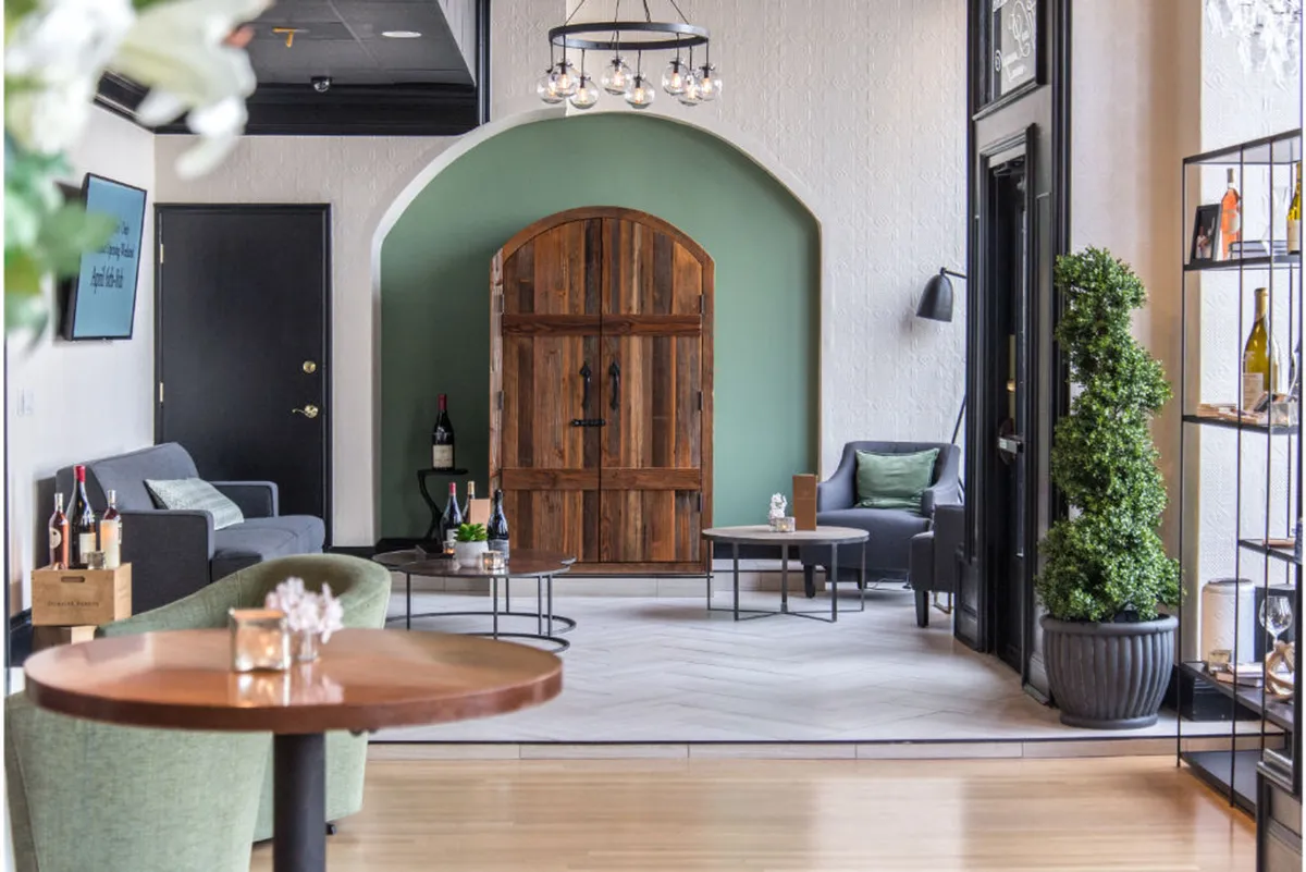 An inviting interior scene featuring a cozy seating area with a green accent wall, wooden door, decorative shelves, and plush chairs. The mood is intimate yet stylish, ideal for relaxing, quiet conversations, or enjoying in-room dining.
