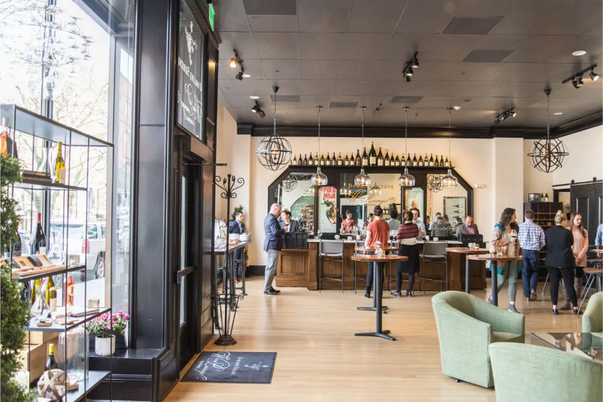 A lively and welcoming interior image of the on-site lounge, highlighting the bar counter, prominent wine displays, and a relaxed seating area. The space suggests opportunities for socializing, relaxing over drinks, or informal networking after work.